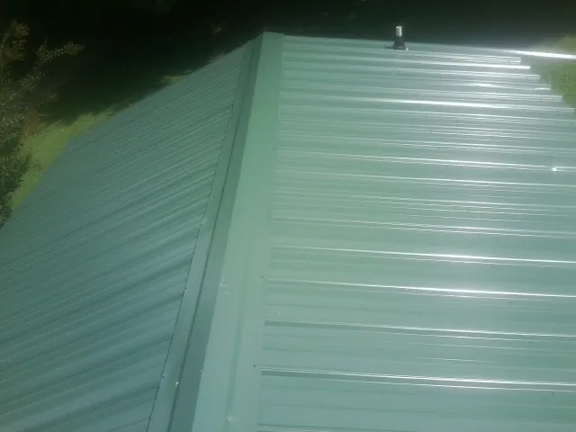 New green metal panels meeting at the ridge of a roof — Flat Roof Repair work by our crew in Cromwell