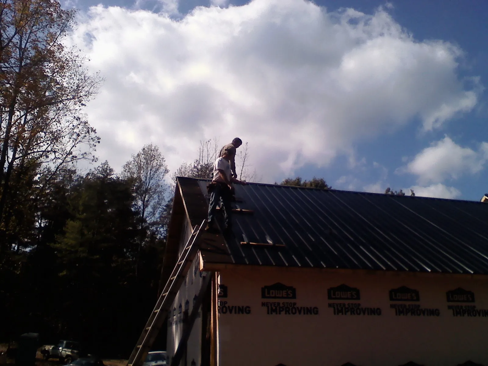 Roofer fastening dark metal panels high against a cloudy sky, from a Roof Inspection job in Cromwell